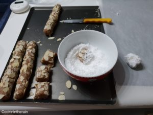 pâte recouverte d'amandes découpée en tronçons puis roulée dans le sucre glace